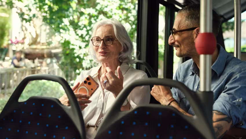 Eine Frau und ein Mann sitzen nebeneinander im Bus und unterhalten sich.