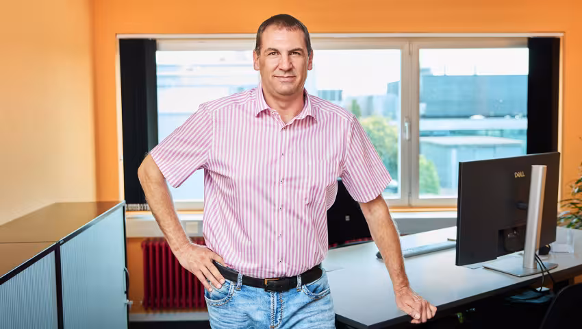 Standortleiter steht in seinem Büro vor dem Schreibtisch.